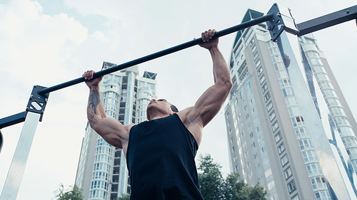 low angle view of tattooed mixed race man exercising on horizontal bar outdoors
