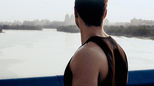 athletic bi-racial man standing on city bridge over river