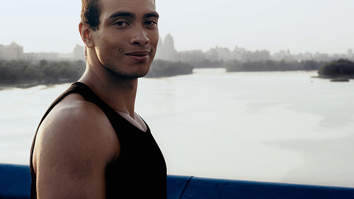 happy bi-racial sportsman  while standing on bridge over river