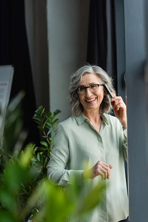 Happy businesswoman in eyeglasses talking on smartphone in office