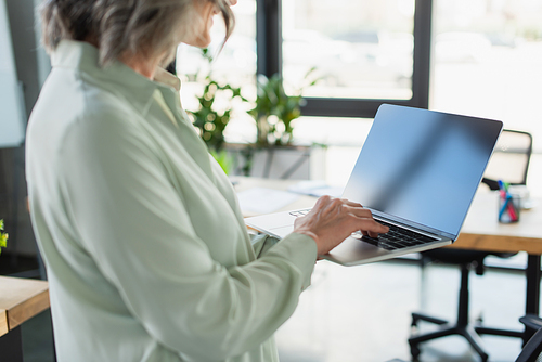 Cropped view of middle aged businesswoman using laptop with blank screen in office