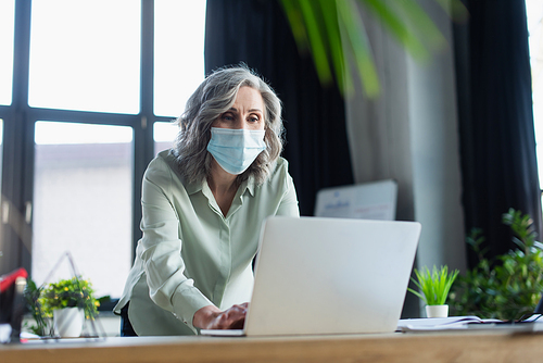 Middle aged businesswoman in medical mask using laptop in office