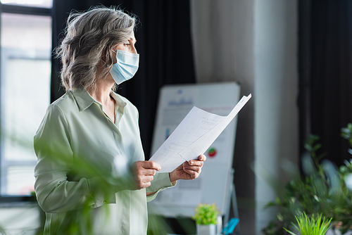 Side view of businesswoman in medical mask holding papers in office