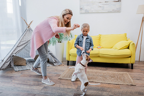 Smiling woman training jack russell terrier near daughter at home