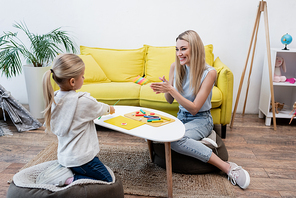 Smiling parent warming plasticine near daughter and coffee table at home