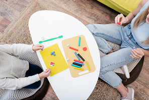 Top view of mother and kid holding plasticine near coffee table at home