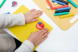 Cropped view of kid holding board near plasticine at home
