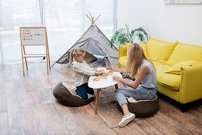 Child and mother playing wood blocks game near couch and teepee at home