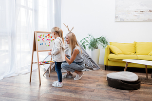 Woman looking at magnetic easel near kid and teepee at home
