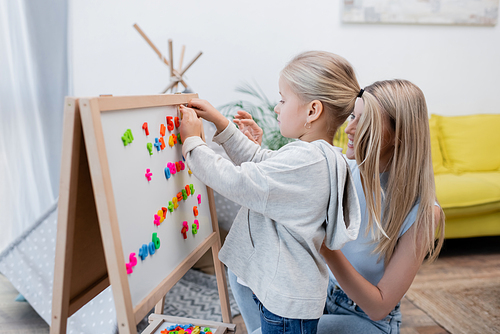 Child fastening colorful magnets on easel near parent at home