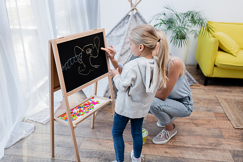Child standing near mother with chalk and chalkboard at home
