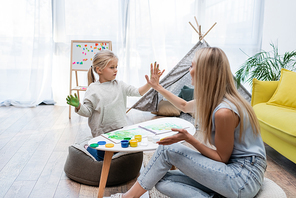 Positive woman and child giving high five while painting at home