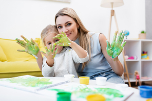 Woman  near daughter looking at hands in paint at home