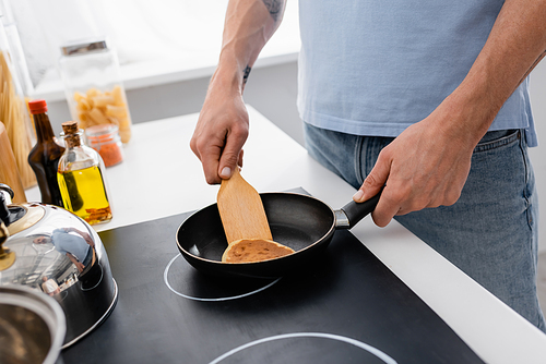 Cropped view of man with spatula cooking pancake in kitchen
