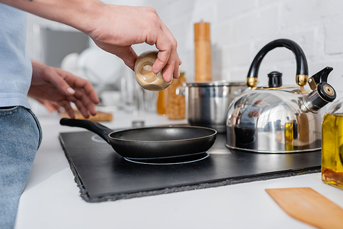 Cropped view of man holding spice near frying pan on stove in kitchen