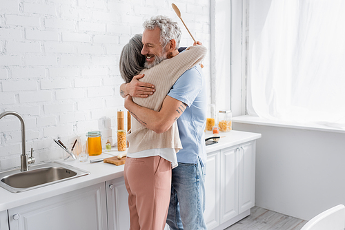 Smiling man hugging wife with spoon in kitchen