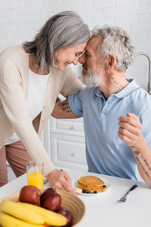 Side view of mature couple smiling near breakfast on table in kitchen