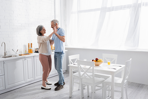 Smiling middle aged couple dancing in kitchen