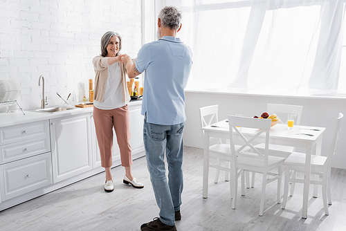 Positive woman holding hand of mature husband in kitchen
