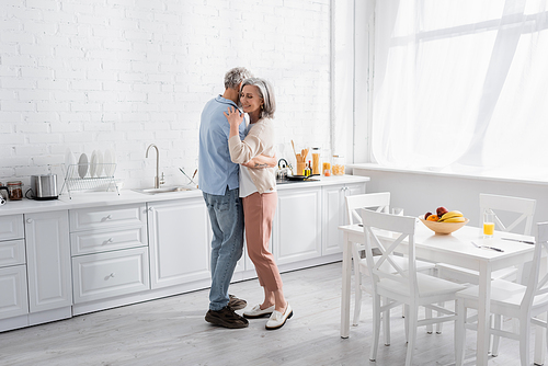 Positive woman hugging husband near fruits and orange juice in kitchen