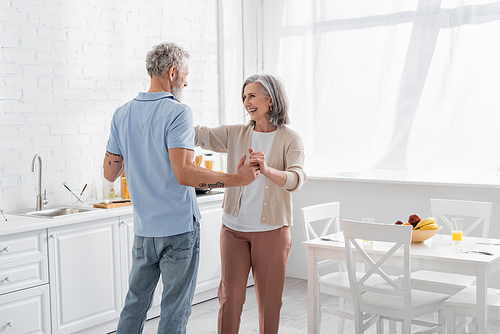 Positive woman holding hand of tattooed husband near fruits on table in kitchen