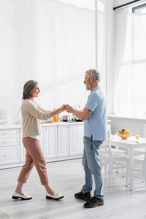 Side view of middle aged couple dancing near fruits and orange juice on table