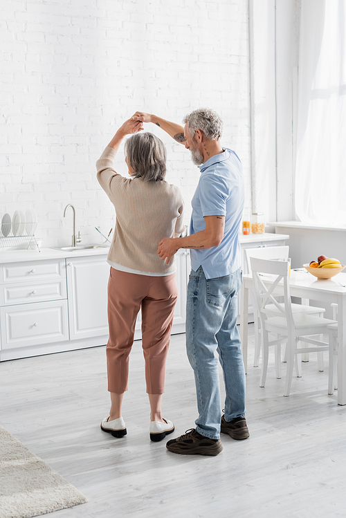 Mature couple dancing near fruits on table in kitchen