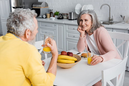 Happy woman looking at blurred husband near breakfast at home