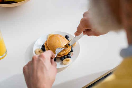 Blurred man cutting pancakes with fruits in kitchen