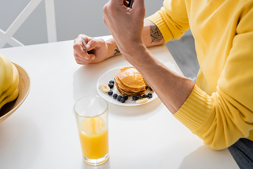 Cropped view of mature man holding knife near pancakes and orange juice in kitchen