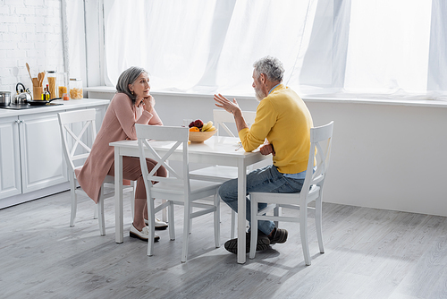 Mature couple talking near fruits in kitchen at home