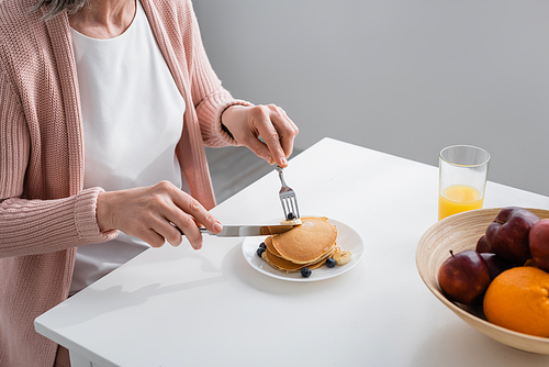 Cropped view of woman cutting pancakes near fresh fruits and orange juice in kitchen