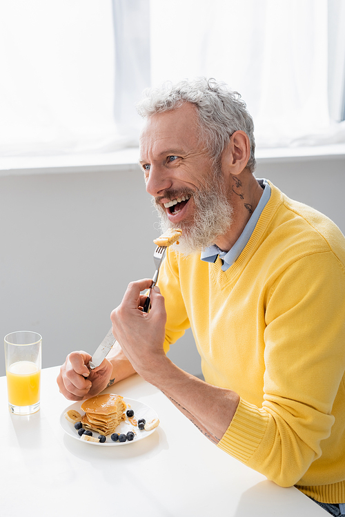 Smiling man eating delicious pancakes in kitchen