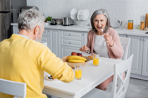 Mature woman eating pancakes during breakfast with husband in kitchen