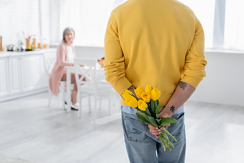 Man holding flowers near blurred wife in kitchen