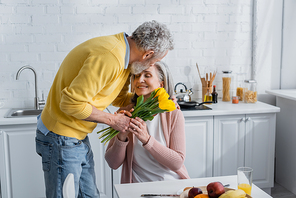 Man presenting flowers to smiling wife near fruits in kitchen