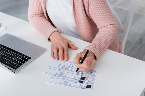 Cropped view of woman writing on bill near laptop at home