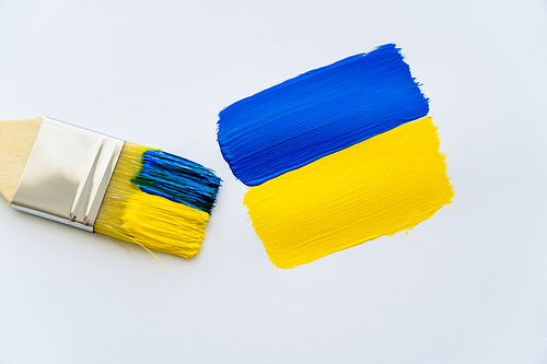 Top view of paintbrush near painted ukrainian flag on white background