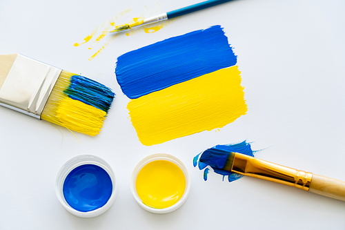 Top view of painted ukrainian flag near paints and paintbrushes on white background