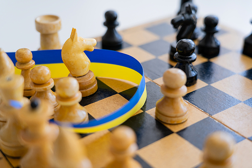 Close up view of blue and yellow ribbon near chess figures on board isolated on white