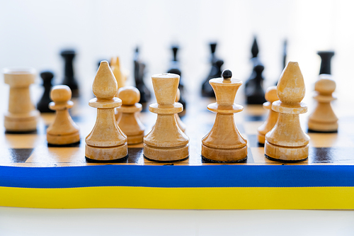 Close up view of blue and yellow ribbon near chess on chessboard on white background