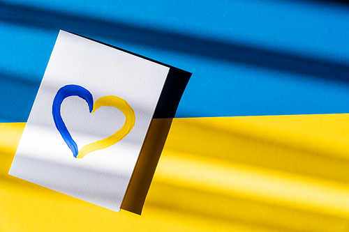 Top view of painted yellow and blue heart sign on card on ukrainian flag