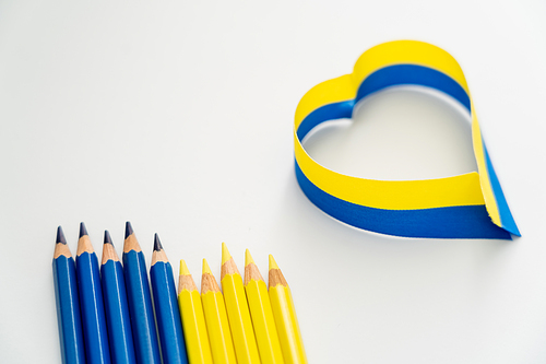 Top view of blue and yellow pencils near ribbon in heart sign on white background