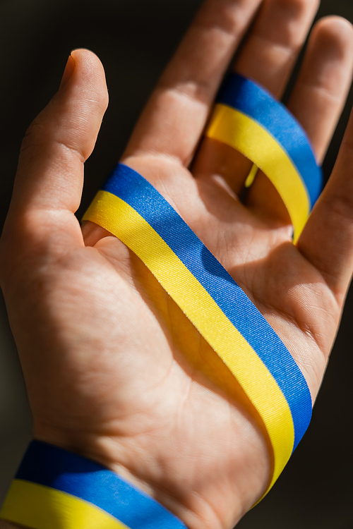 Cropped view of blue and yellow ribbon on blurred male hand on black background