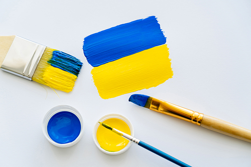 Top view of painted ukrainian flag near paintbrushes and paints on white background