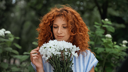 curly redhead woman looking at bouquet of white flowers