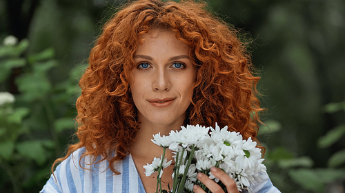 curly redhead woman with blue eyes holding bouquet of white flowers
