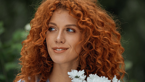 curly redhead woman with blue eyes near white flowers
