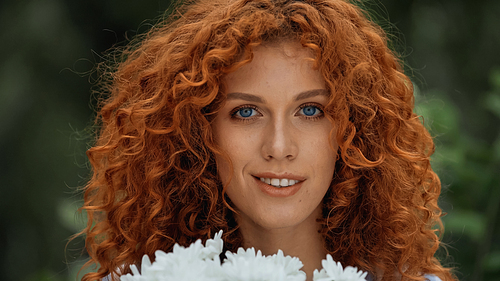 smiling redhead woman with blue eyes near white flowers