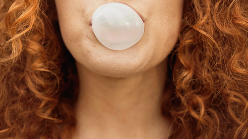 cropped view of curly woman blowing bubble gum
